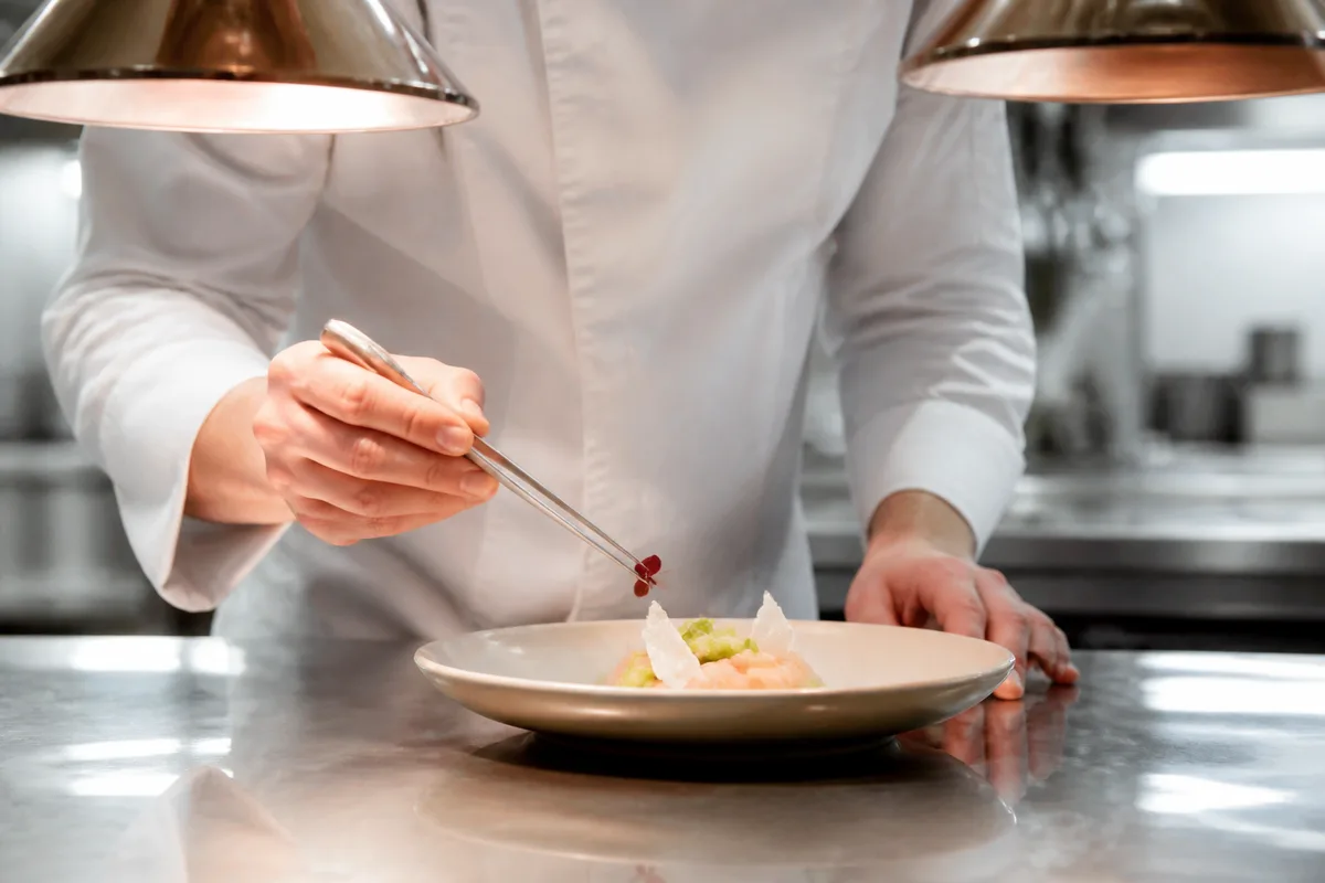Chef en veste blanche dressant une assiette gastronomique au passe
